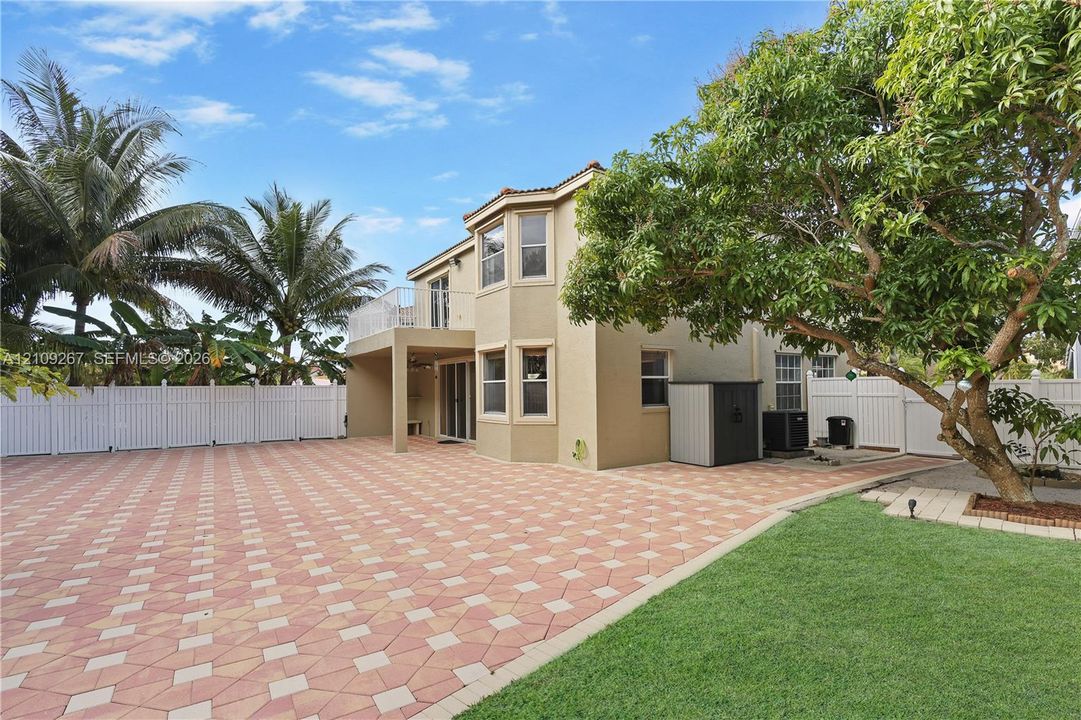 Multi-level exterior featuring a paved patio, second-story balcony, fenced perimeter, and mature landscaping