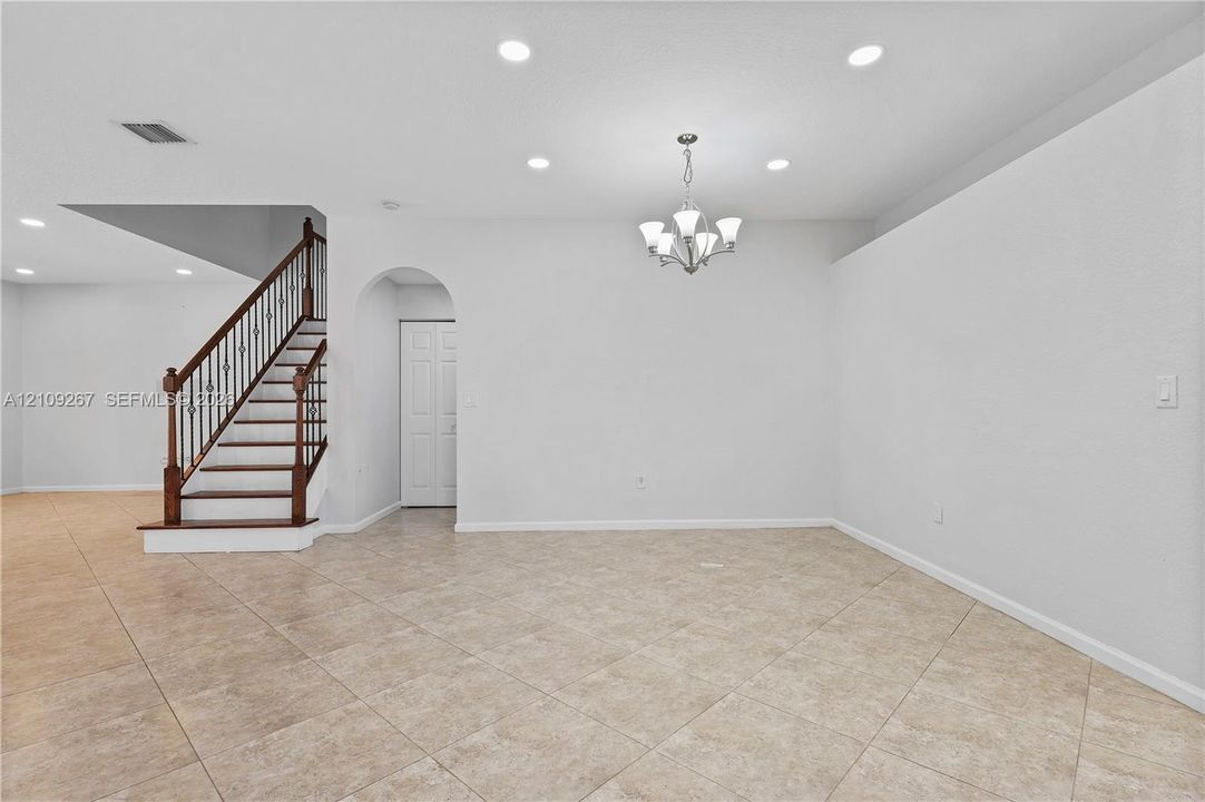 Interior space featuring large-format tile flooring, recessed lighting, a multi-arm chandelier, and a staircase with wood treads and decorative metal balusters