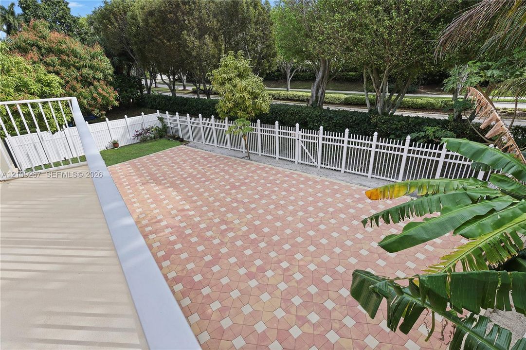 Elevated patio with stone paver flooring, white vinyl fencing, and perimeter hedging
