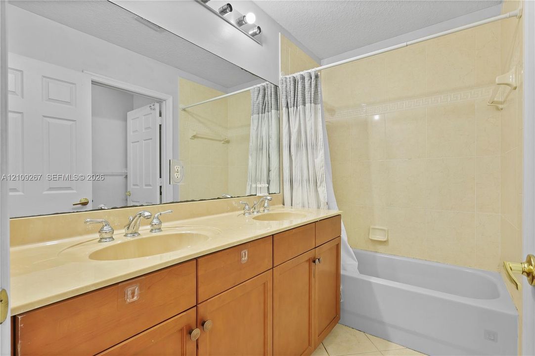 Dual-sink vanity with integrated countertop, large wall-mounted mirror, three-light fixture, and tub-shower combination with tiled surround