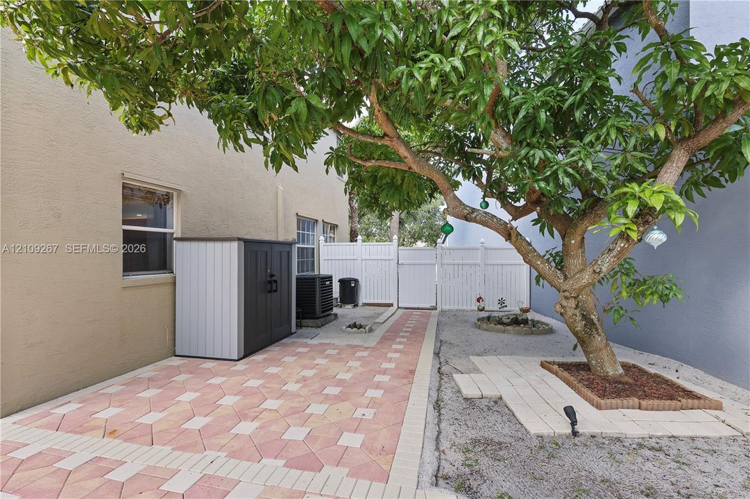 Side yard featuring a paver-stone patio, a mature tree with a brick-bordered planting bed, and a privacy fence