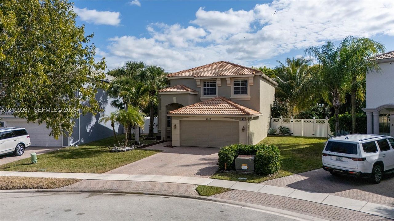Two-story stucco exterior featuring a tiled hip roof, integrated two-car garage, paved driveway, and established landscaping