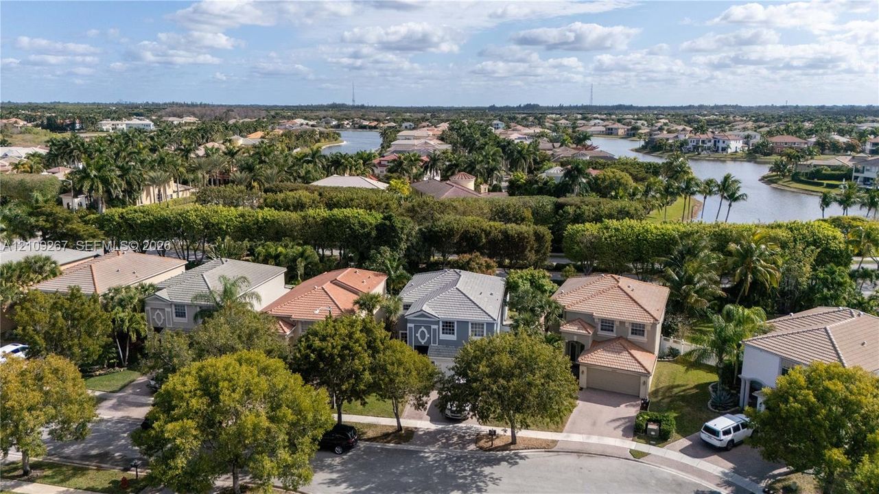 Aerial perspective of a residential neighborhood featuring paved streets, mature trees, multi-roofline structures, and waterways
