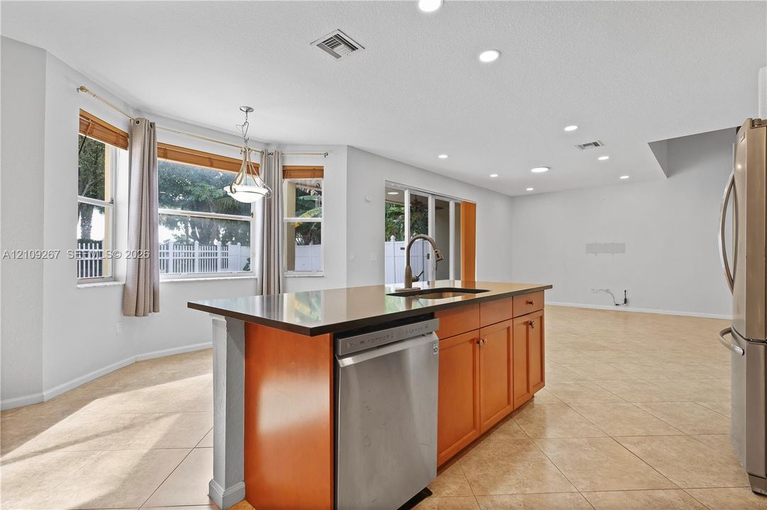 Kitchen featuring a central island with a dark solid-surface countertop, stainless steel dishwasher, wood-finish cabinetry, recessed lighting, and tile flooring
