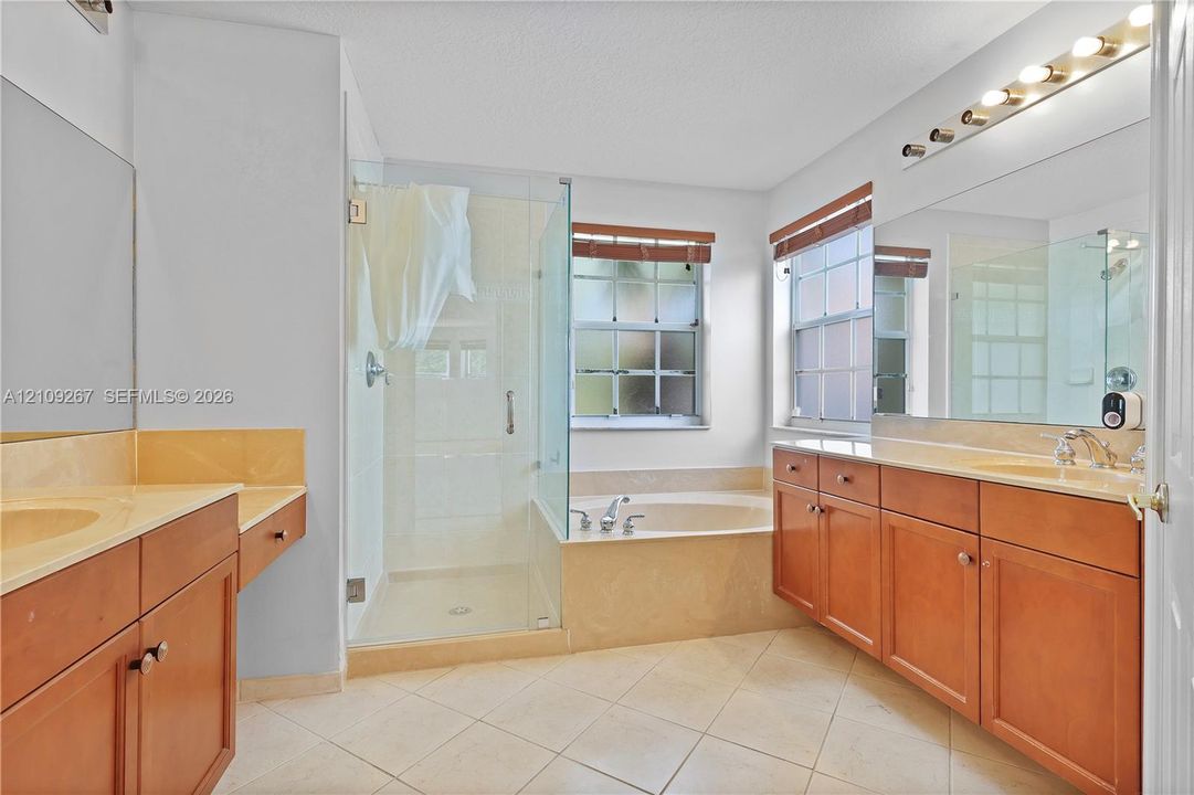 Bathroom featuring a large vanity with stone-style countertops, a glass-enclosed shower, a deep soaking tub with a tiled surround, multi-light fixture, and ceramic tile flooring