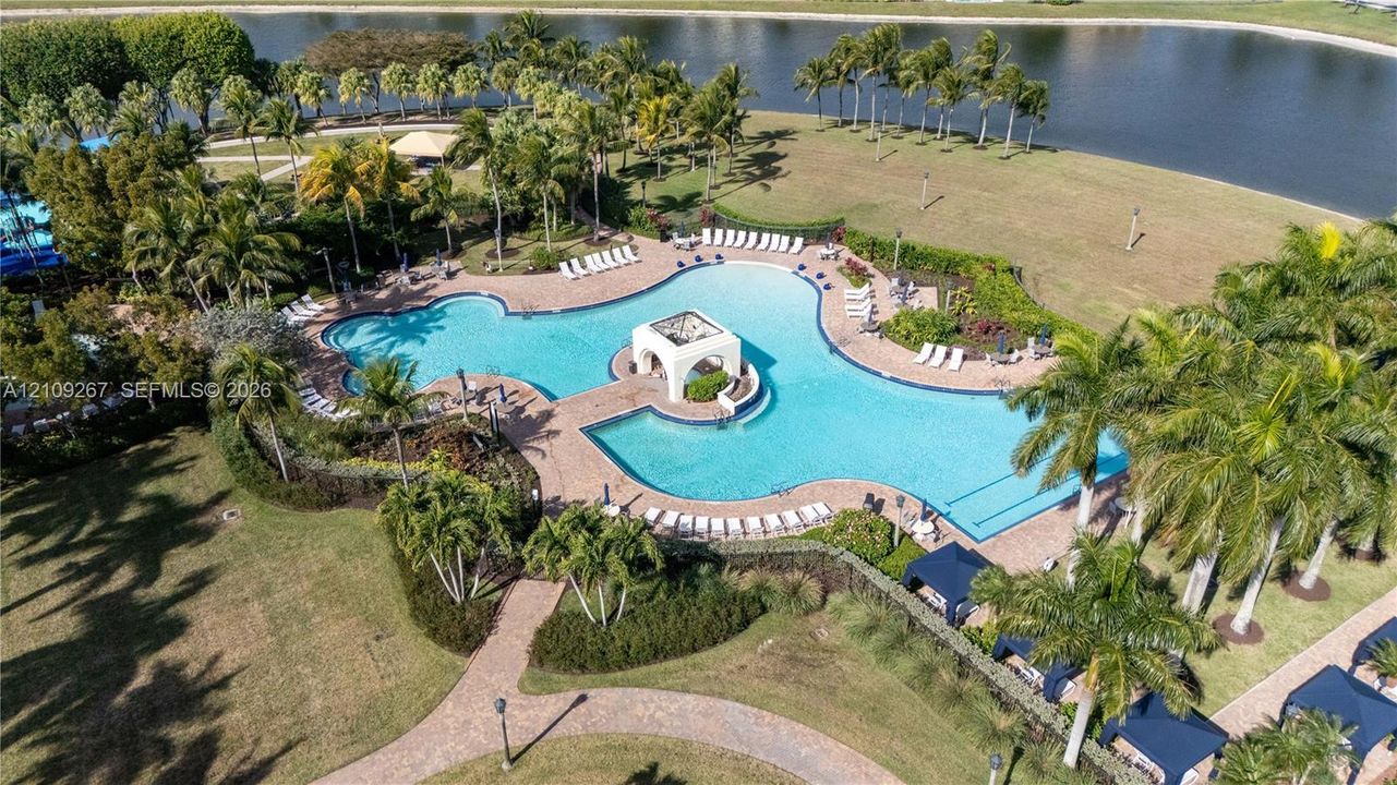 Expansive lagoon-style swimming pool featuring a central architectural pavilion, brick-paver decking, and waterfront positioning