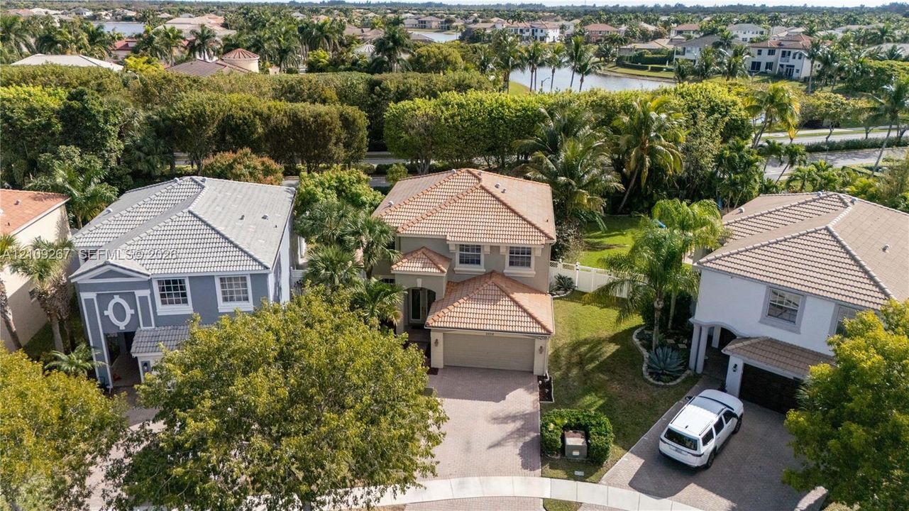Two-story residential structure featuring a multi-gabled tile roof, stucco exterior, paved driveway, and established perimeter landscaping