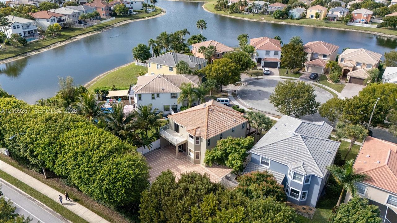 Aerial perspective of a two-story residence featuring a tile roof, a paved patio, a balcony, and direct waterfront access