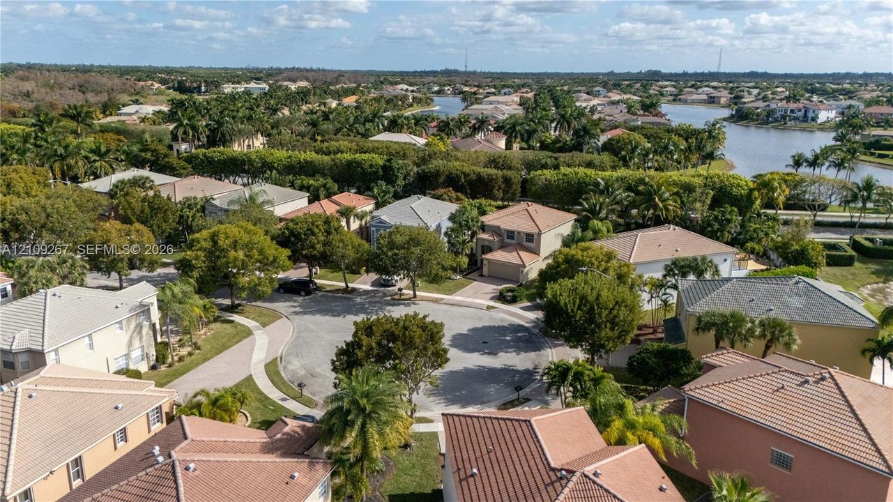 Aerial perspective of a cul-de-sac community featuring tile roofing, paved driveways, established trees, and proximity to a neighborhood lake