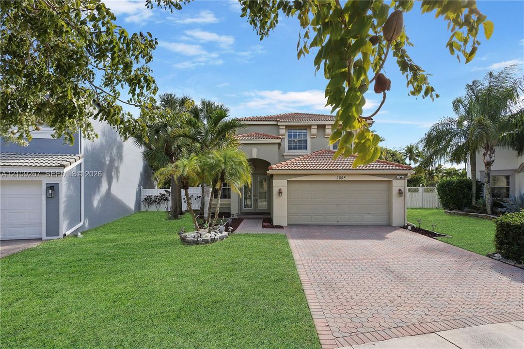 Two-story residence featuring a terracotta-tiled roof, stone-paver driveway, stucco exterior, and mature palms