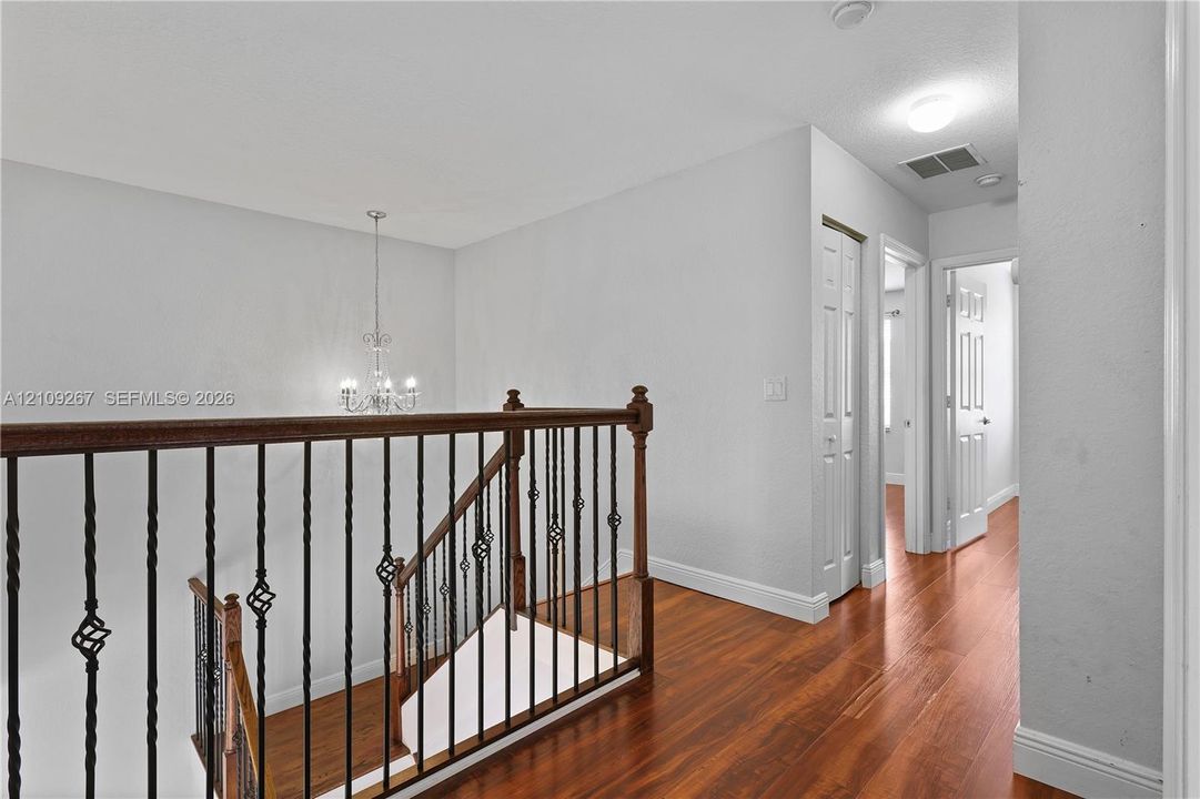 Staircase featuring wood-finish flooring, metal balusters with decorative twists, and a wood handrail, accented by a multi-bulb chandelier