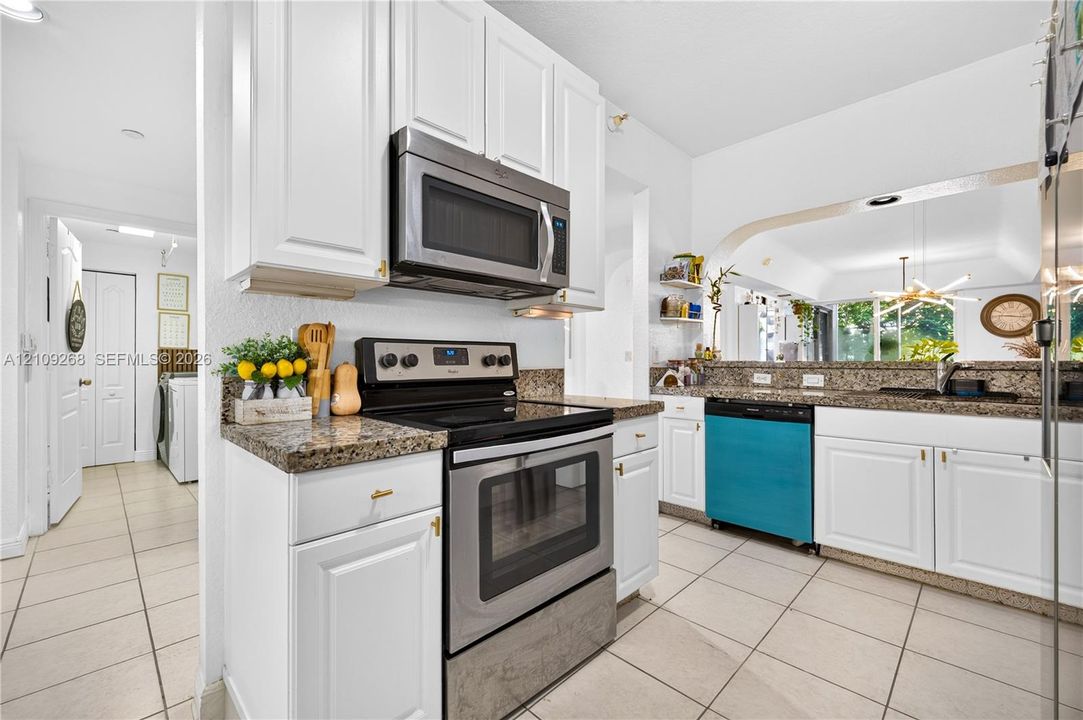 Kitchen featuring white Shaker-style cabinetry, stone-finish countertops, stainless steel appliances, and ceramic tile flooring