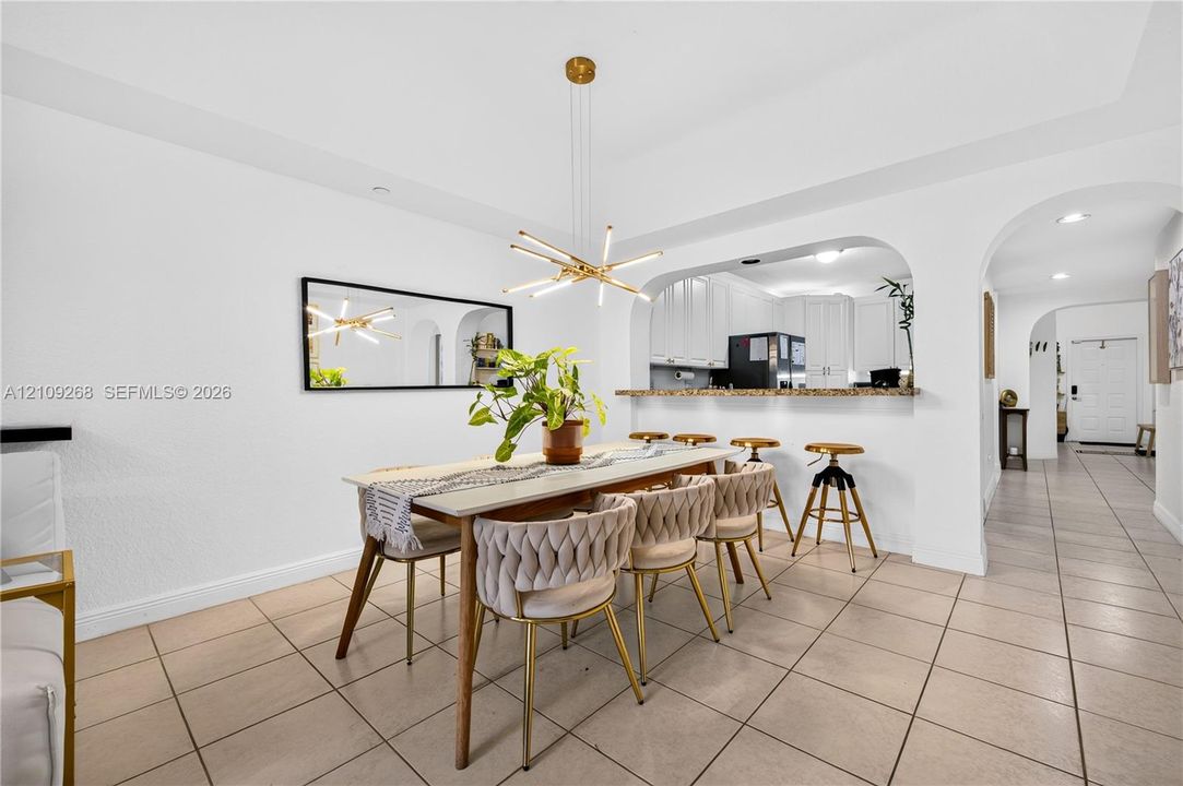 Dining area featuring tile flooring, a multi-light contemporary chandelier, arched architectural detailing, and a breakfast bar with stone-surface countertop