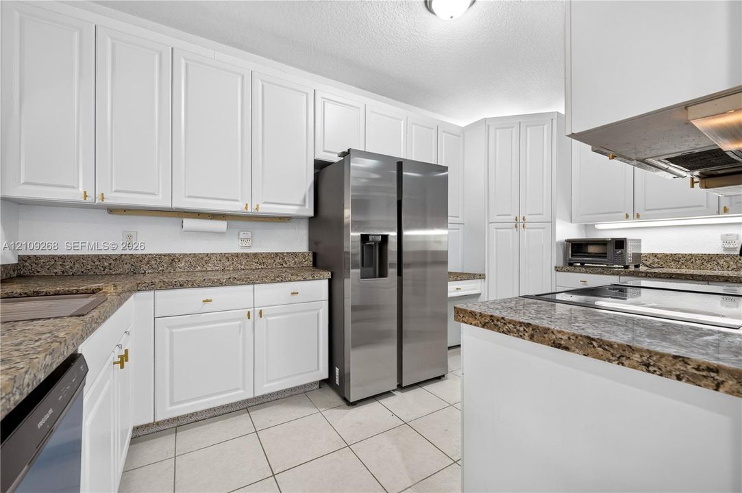 Kitchen featuring white cabinetry, stone-surface countertops, tile flooring, and stainless steel appliances