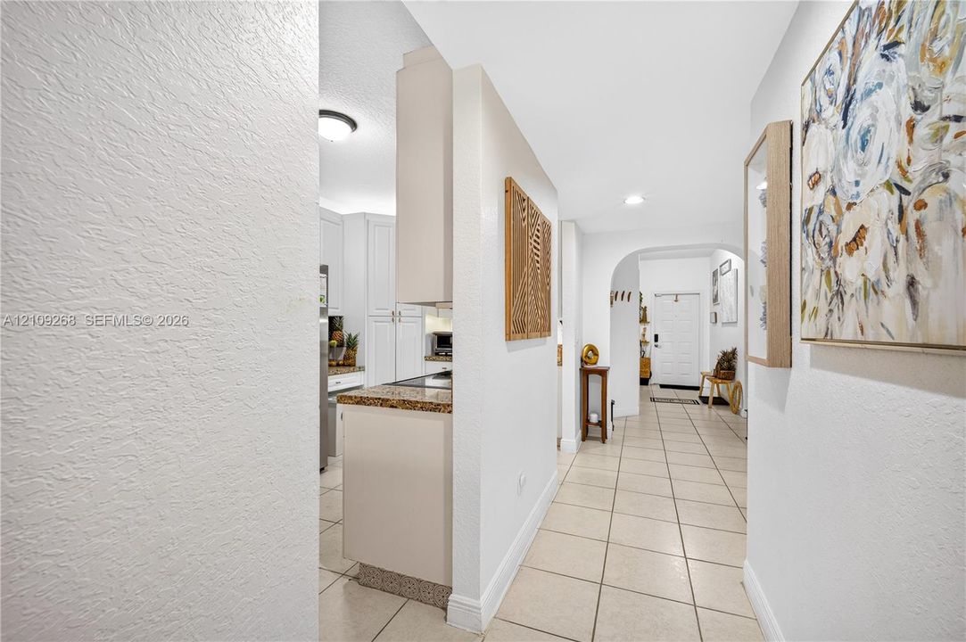 Interior hallway featuring light-toned tile flooring, white textured walls, recessed ceiling lighting, and a distinct arched entryway