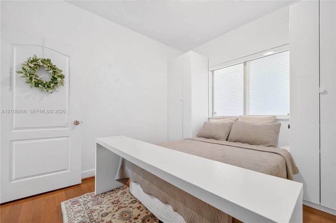 Interior room featuring wood-finish flooring, white paneled door, and built-in white wardrobe cabinetry