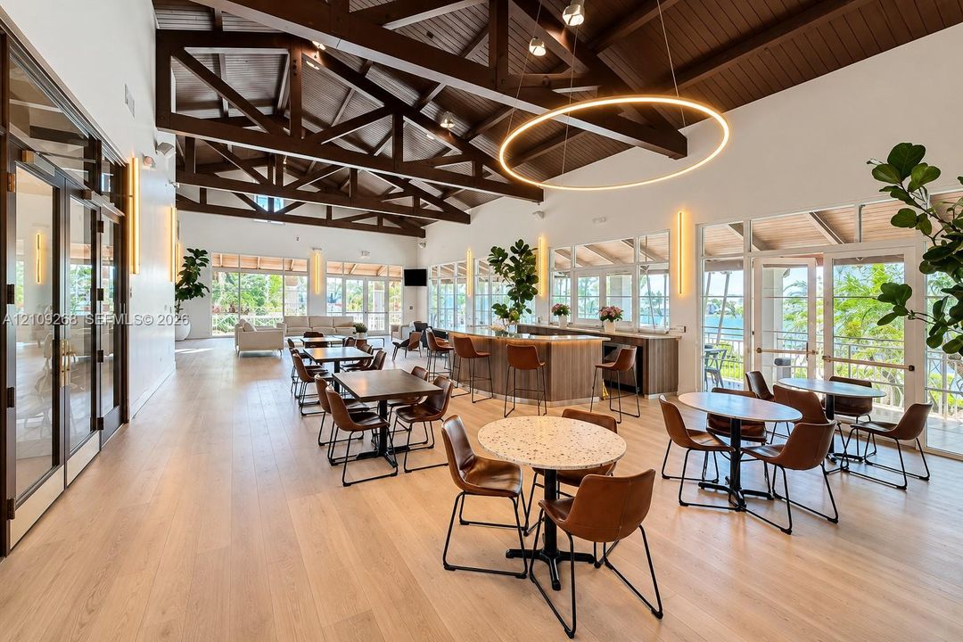 Open-concept interior featuring exposed wood-truss vaulted ceilings, wood-finish flooring, a built-in refreshment bar with quartz countertop, and expansive glass-paned doors