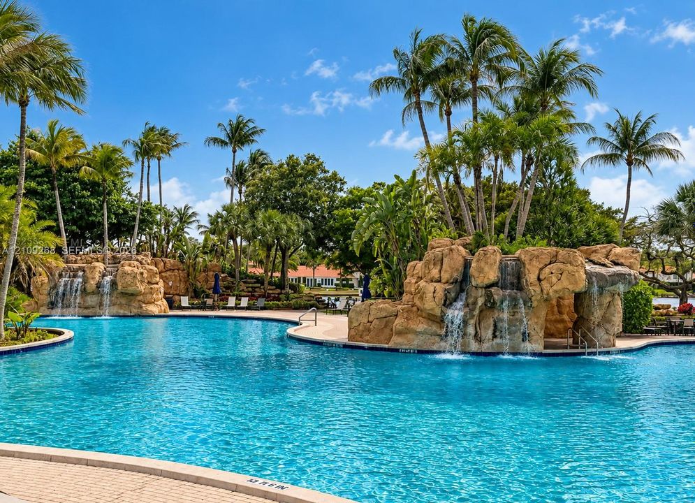 Swimming pool featuring integrated rock formations, multiple cascading waterfalls, and palm tree landscaping