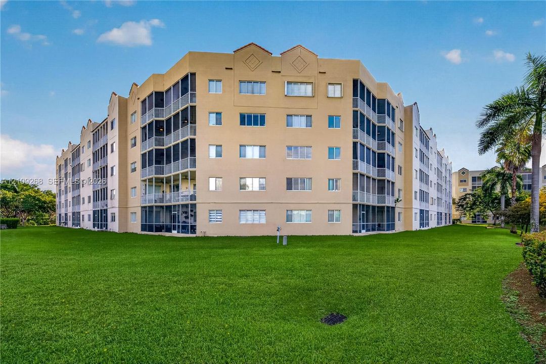 Multi-story residential building featuring a stucco exterior, integrated screened-in balconies, and expansive surrounding lawn areas
