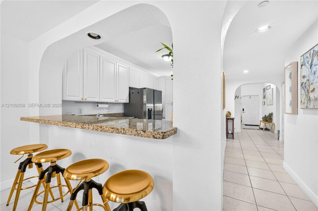 Kitchen featuring white cabinetry, stone-surface breakfast bar, recessed lighting, and arched architectural entryways with tile flooring
