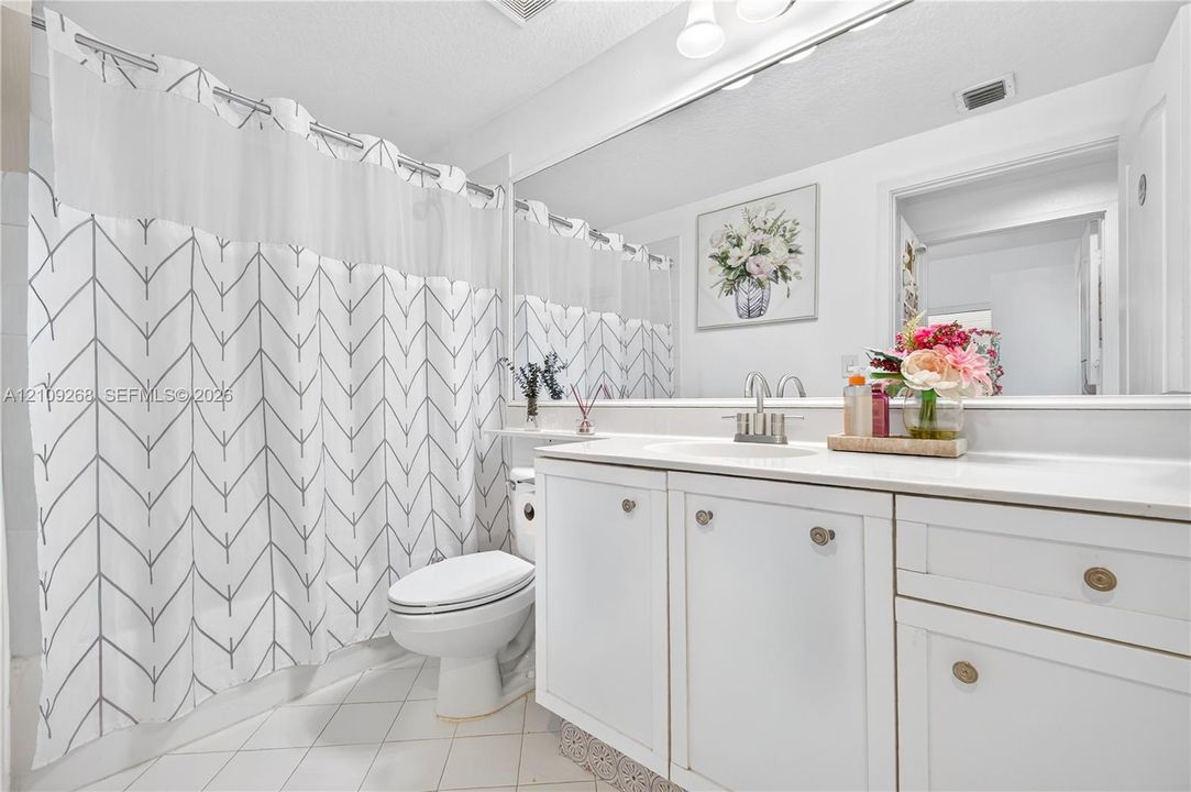 Bathroom featuring white cabinetry, an integrated basin, a large wall-mounted mirror, and tile flooring