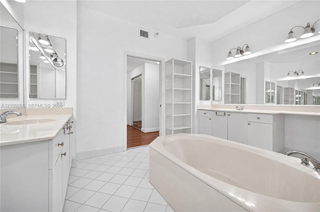 Dual-sink vanity with light-toned solid surface countertops, built-in shelving, large wall-mounted mirrors, and an expansive soaking tub