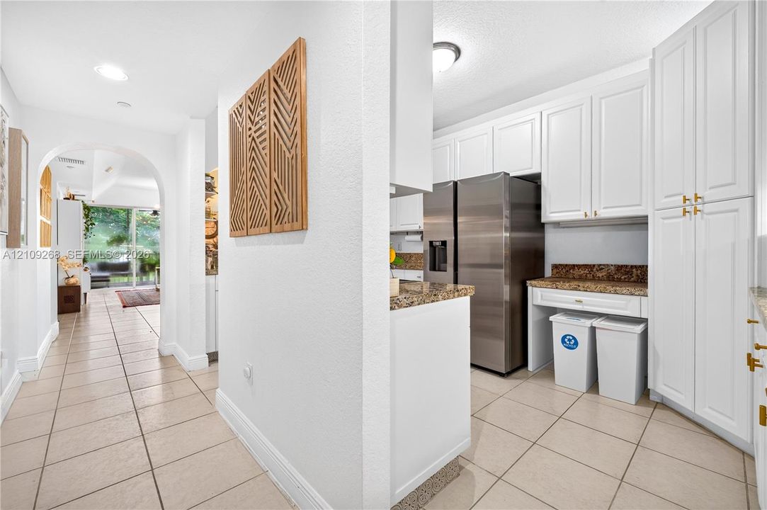 Kitchen featuring white shaker-style cabinetry, stone-surface countertops, recessed lighting, tile flooring, and a stainless steel refrigerator