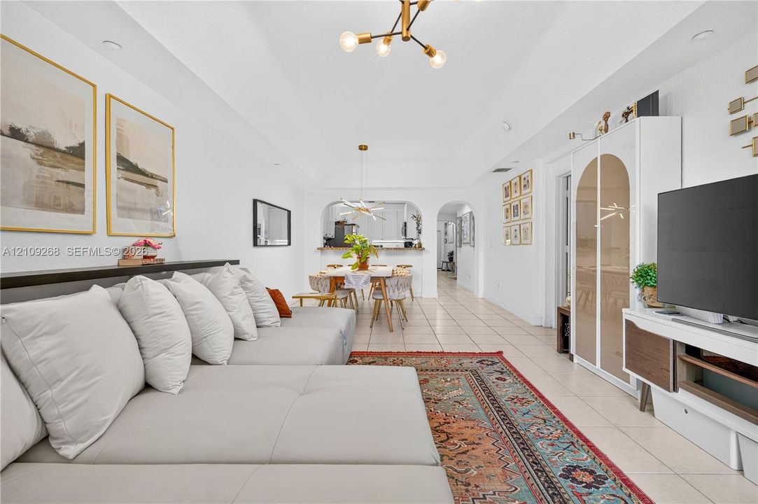 Tray ceiling, neutral tile flooring, modern multi-arm chandelier lighting, and arched architectural wall opening