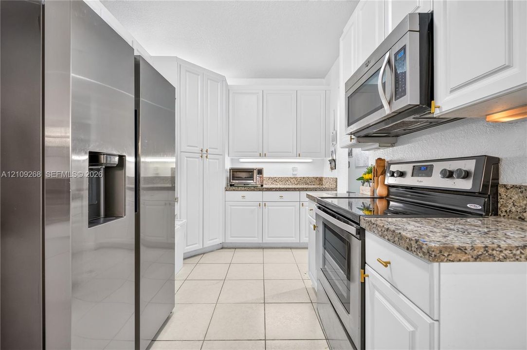 Kitchen featuring white cabinetry, stone-finish countertops, stainless steel appliances, and tile flooring