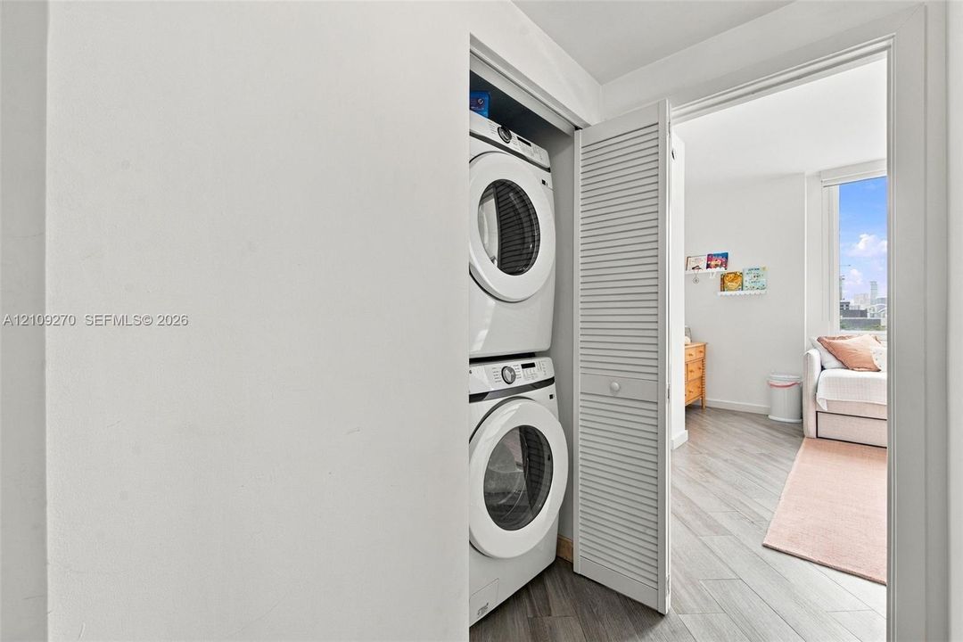 Laundry closet featuring a stackable washer and dryer unit enclosed by white louvered bi-fold doors