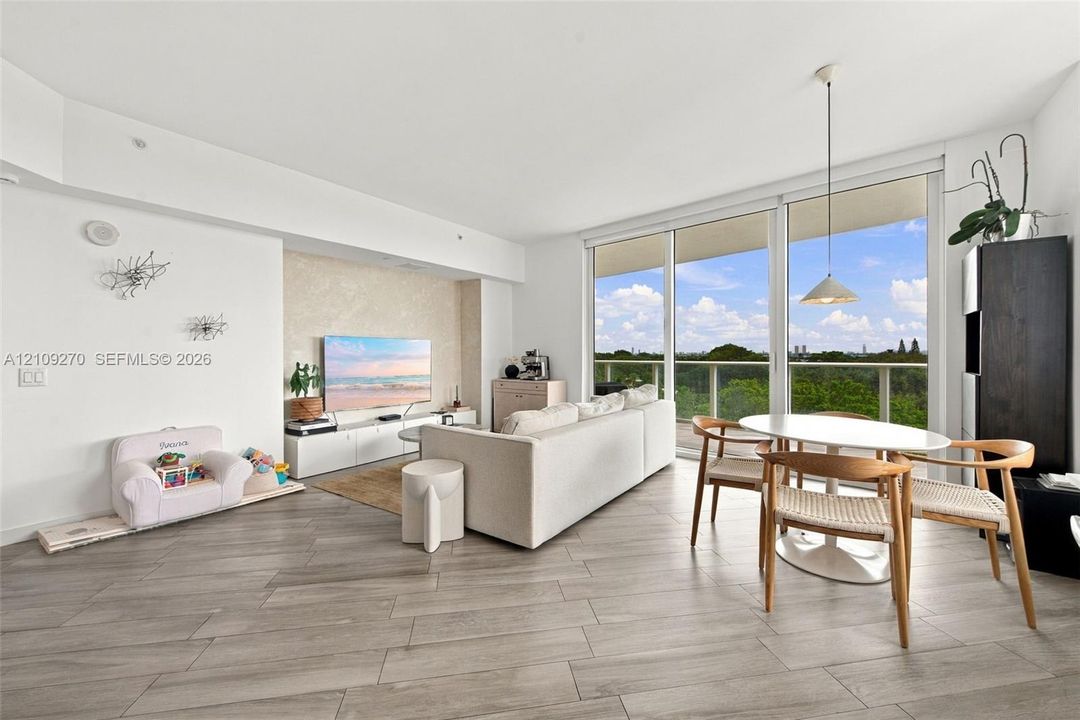 Open-concept living space featuring wood-finish flooring, floor-to-ceiling glass sliding doors, a balcony, and a recessed accent wall with built-in media cabinetry