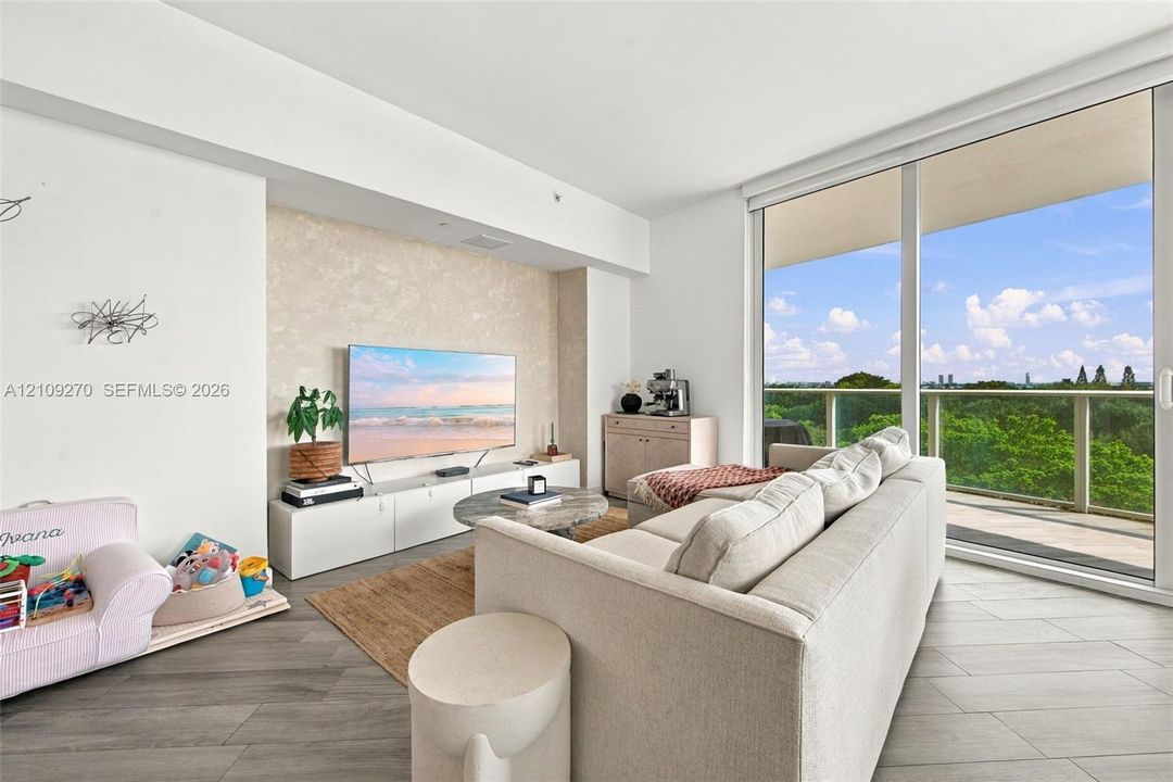 Floor-to-ceiling sliding glass doors, spacious balcony with glass railing, wood-finish flooring, and a textured accent wall