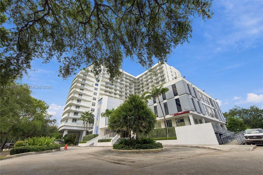 Multi-story building exterior featuring a white concrete facade, recessed private balconies, and panelized metal cladding