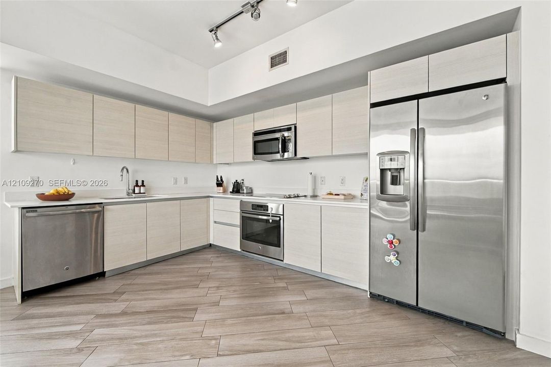 Kitchen featuring flat-panel cabinetry, light-toned countertops, stainless steel appliances, and plank-style flooring with integrated track lighting
