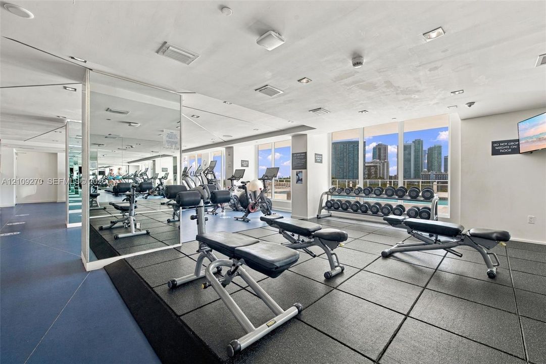 Fitness center featuring full-height wall mirrors, rubberized tile flooring, floor-to-ceiling windows, and recessed ceiling lighting