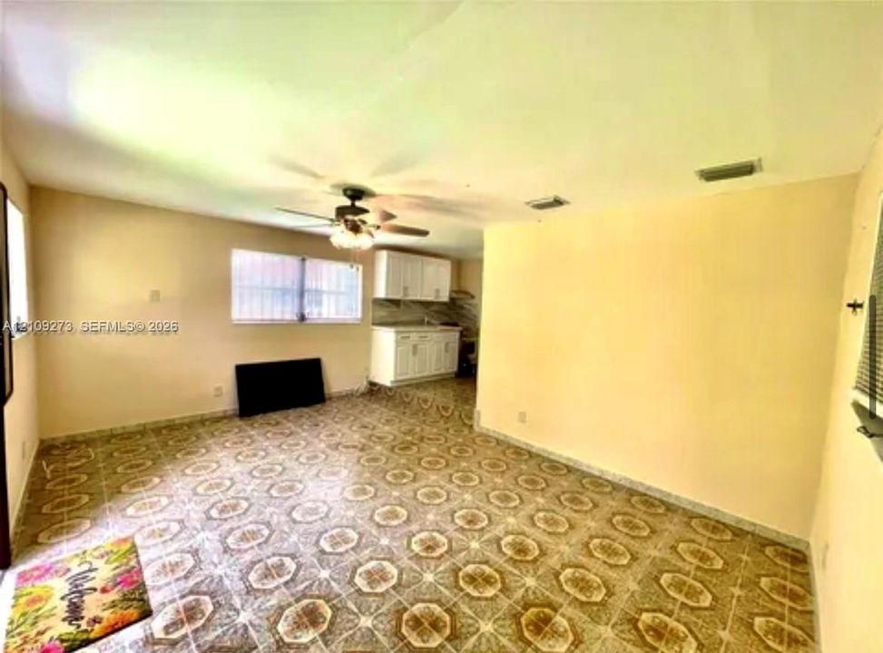 Open-concept interior featuring patterned tile flooring, white cabinetry, a multi-blade ceiling fan, and large windows