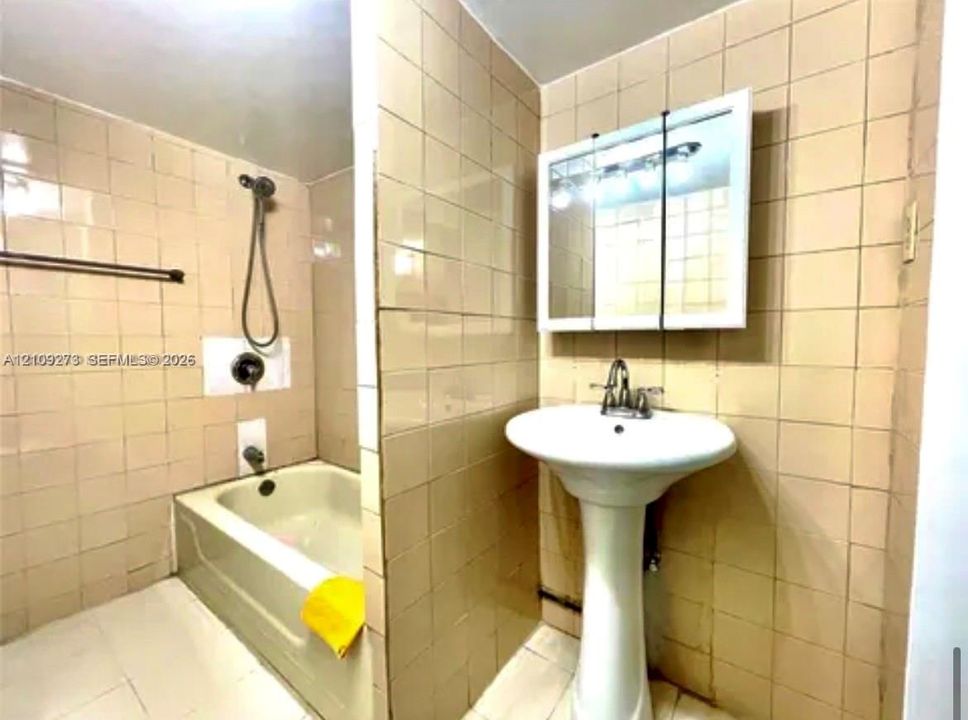 Pedestal sink with polished chrome faucet, wall-mounted mirrored medicine cabinet, built-in bathtub with integrated shower head, and full-height tiled wall surfacing