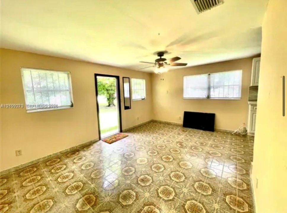 Open-concept space featuring patterned tile flooring, a ceiling fan with integrated lighting, exterior door with glass insert, and multiple windows with security bars