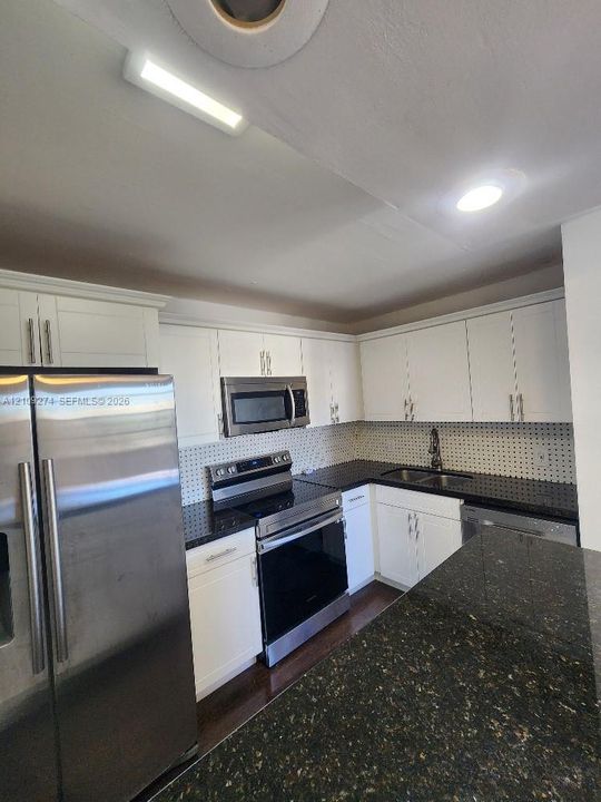 Kitchen featuring white shaker-style cabinetry, dark stone countertops, stainless steel appliances, a tiled backsplash, and recessed lighting
