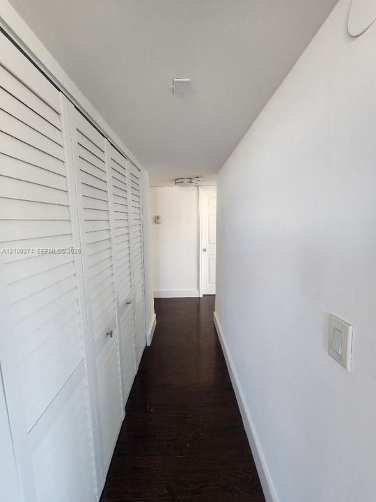 Hallway featuring dark wood-finish flooring, white walls, and built-in closet storage with louvered doors