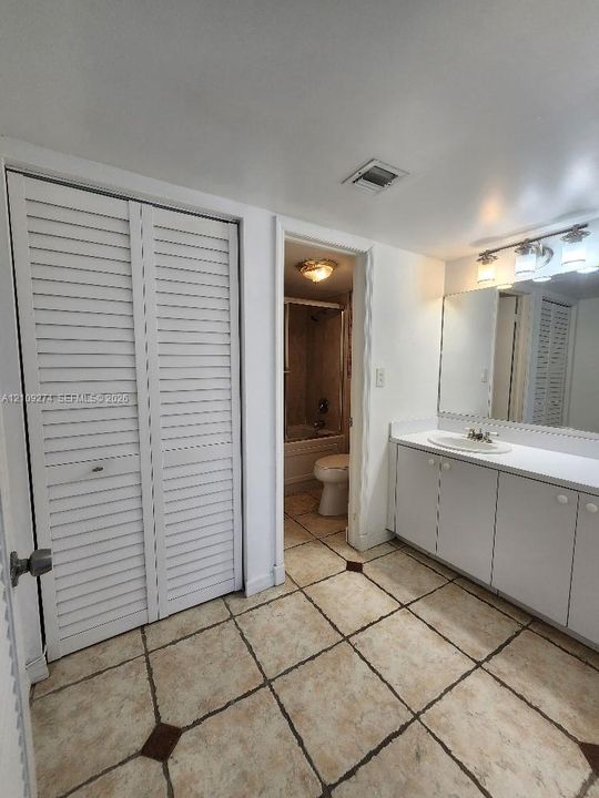 Bathroom featuring a vanity with a solid-surface countertop and integrated sink, a full-width wall-mounted mirror, louvered-door closet cabinetry, and tile flooring with decorative accent inlays
