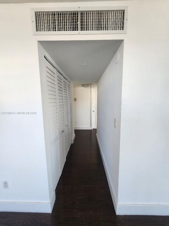 Hallway featuring dark wood-finish flooring, white louvered closet doors, and a ceiling-mounted light fixture