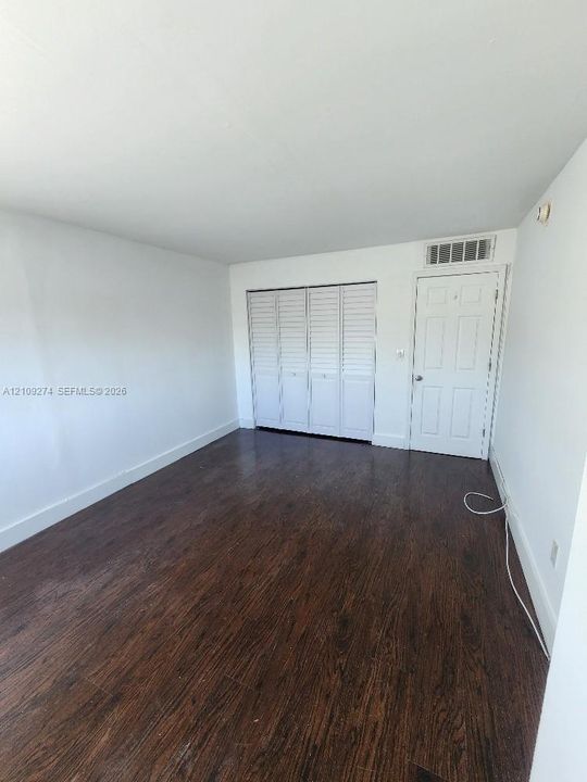 Room featuring wood-finish flooring, white walls, and a four-panel louvered closet door