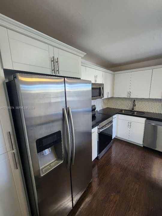 Kitchen featuring white shaker-style cabinetry, stainless steel appliances, dark stone-finish countertops, mosaic tile backsplash, and dark wood-finish flooring