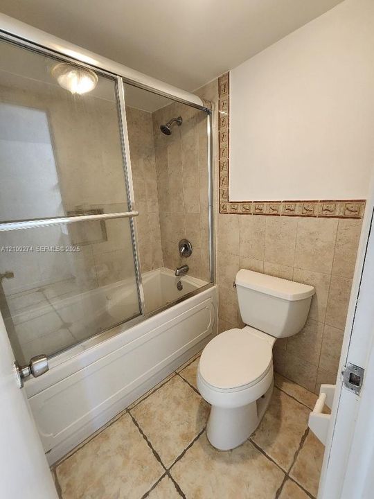Full bathroom featuring a tub-shower combination with sliding glass doors, neutral tile flooring, tile surround with decorative accent inlay, and a two-piece toilet