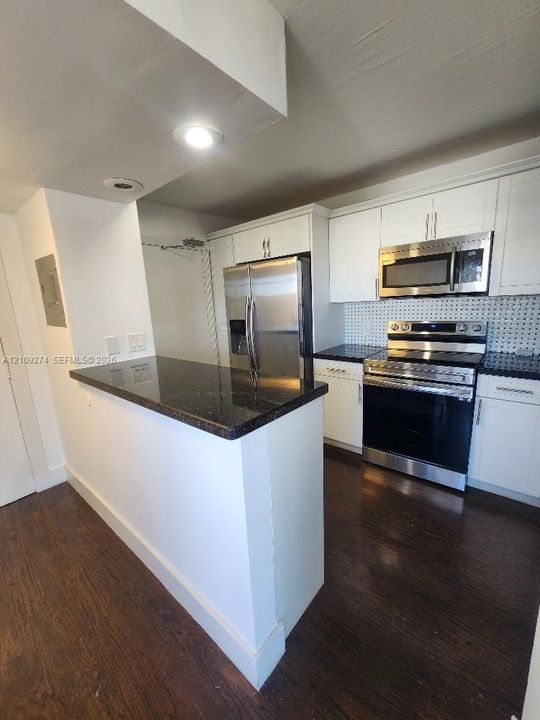 Kitchen featuring white cabinetry, dark stone countertops, stainless steel appliances, a mosaic-tile backsplash, and wood-finish flooring