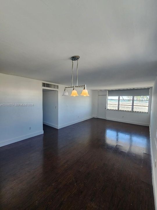 Open-concept interior featuring dark wood-finish flooring, a multi-light brushed-metal chandelier, and expansive windows with exterior water scenery