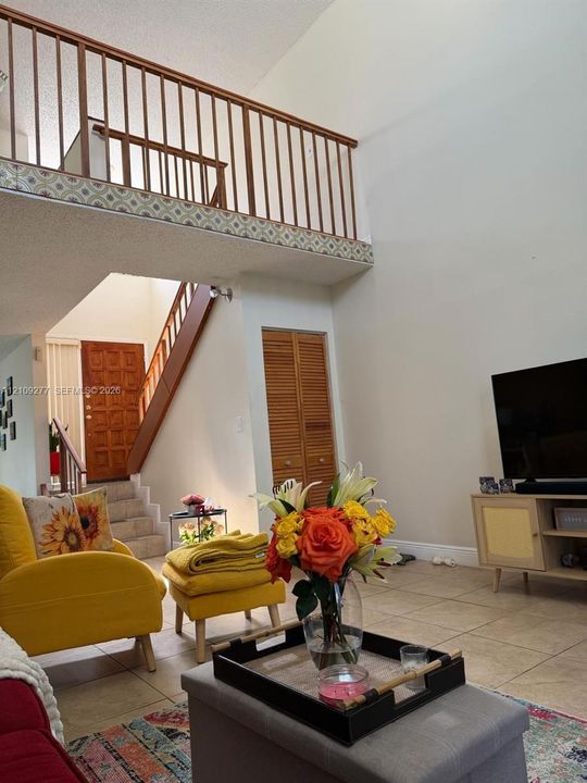 Vaulted ceilings featuring a mezzanine level with decorative railings, tiled flooring, and wooden staircase architecture