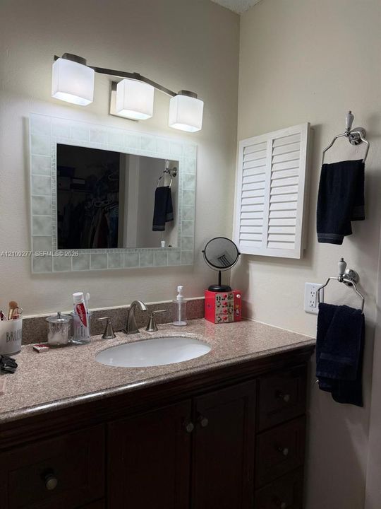Vanity featuring a dark-finish wood cabinet, speckled stone-surface countertop, an oval undermount sink with a widespread faucet, a tile-framed mirror, and a three-light fixture with frosted glass shades