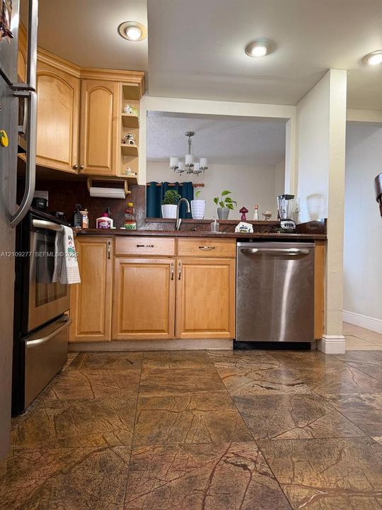 Kitchen featuring light wood cabinetry, stone-finish countertops, stainless steel appliances, and patterned tile flooring